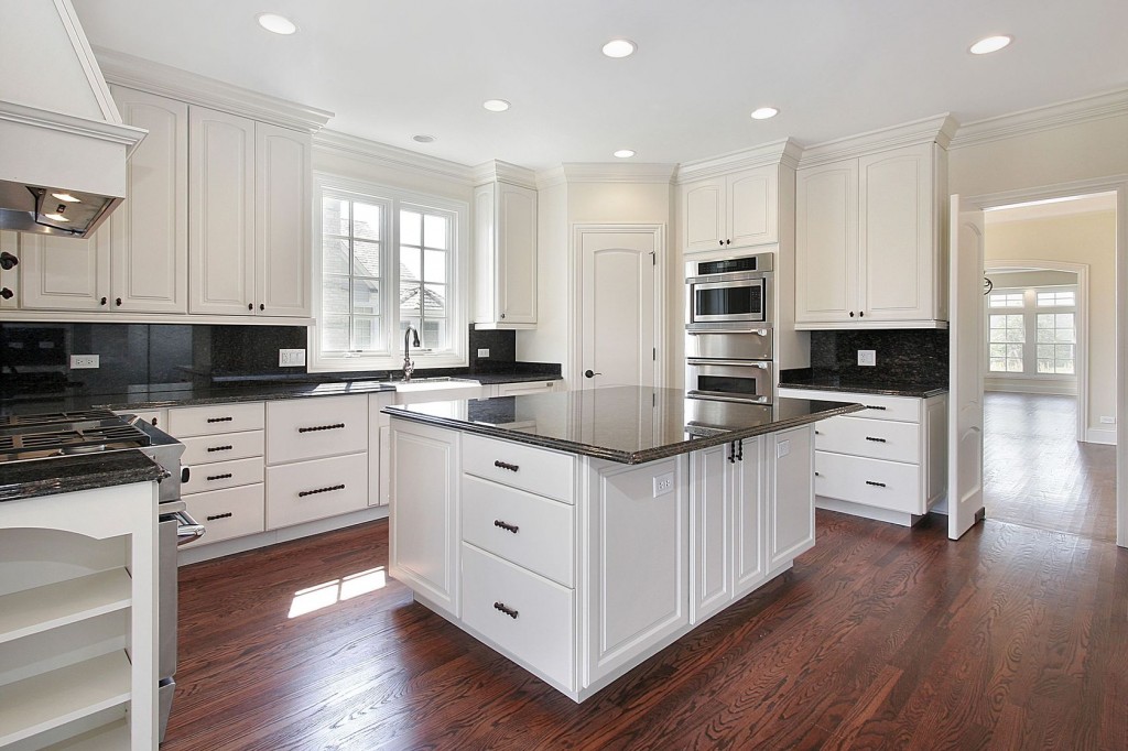 A kitchen with white cabinets and black counter tops.